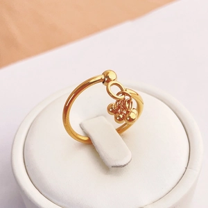Minimalist gold open ring with hanging metallic beads on a white circular display stand