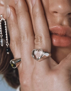Vue détaillée d'une bague coeur argentée et d'une bague avec pierre verte au doigt