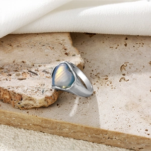 Détail de la bague coeur argentée avec pierre à effet irisé sur support en pierre