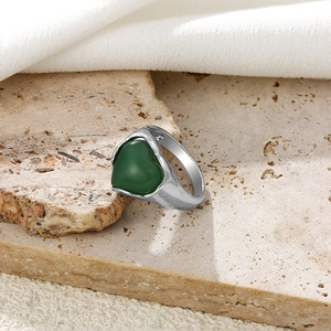 Détail d'une bague coeur argentée avec pierre verte sur une surface en pierre