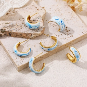 C-shaped 18K gold earrings with blue white enamel marble texture on stone background