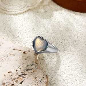 Détail d'une bague coeur en argent avec une pierre de labradorite naturelle sur du sable blanc