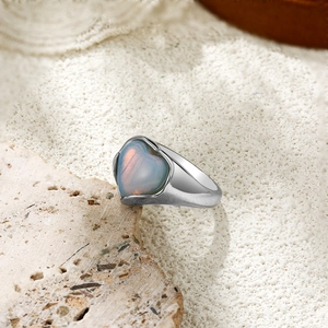 Détail macro de bague coeur en opale argentée avec reflets irisés sur fond de pierre