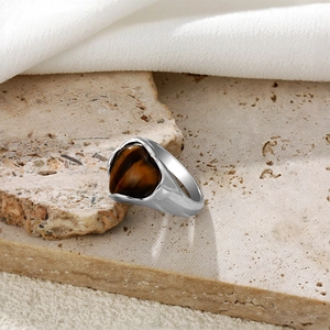 Détail de bague en argent avec pierre oeil de tigre en cœur sur fond de pierre