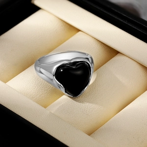 Vue détaillée d'une bague argentée avec une grande pierre noire en cœur sur support beige