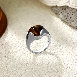 Vue détaillée d'une bague en argent ornée d'un œil de tigre poli sur du sable blanc