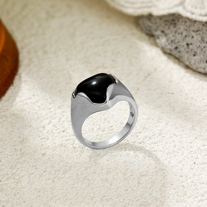 Détail d'une bague en argent avec une grande pierre noire sur fond texturé chic