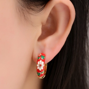 Close-up of a red enamel hoop earring with white flower pattern on a model's ear