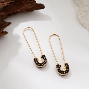Detailed close-up of gold safety pin earrings with black pavé micro-inlaid stones