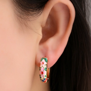 Close-up of golden hoop earrings with colorful floral enamel patterns on a female model