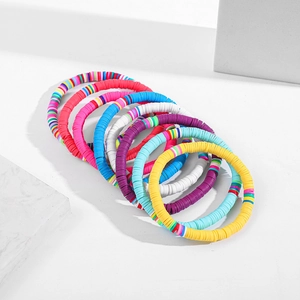 Set aus 10 bunten Boho-Heishi-Perlenarmbändern auf einer weißen Steinoberfläche
