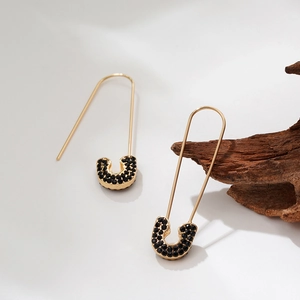 Detailed view of gold safety pin earrings with pave black zircon on white background
