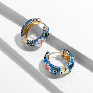 Macro detail of enamel flower earrings with blue glaze and pink blossoms on gold hoops