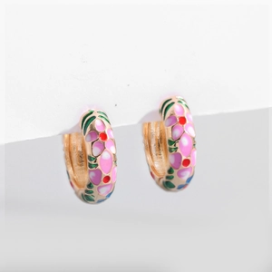 Macro detail of golden hoop earrings featuring colorful enamel flower patterns and green leaves