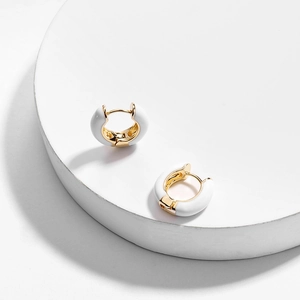 Gros plan de boucles d'oreilles créoles dorées en émail sur un support blanc minimaliste