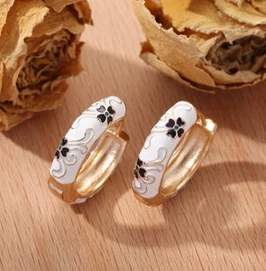 Close-up of gold hoop earrings with white enamel and black floral pattern details