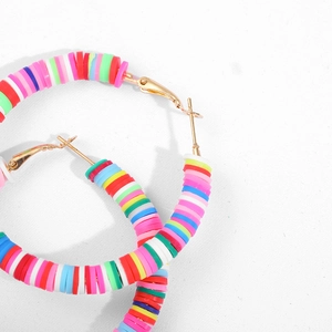 Macro detail of rainbow polymer clay disc beads on gold C-shaped hoop earrings