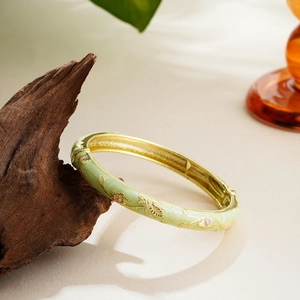 Artistic close-up of light green enamel bangle with gold floral relief on a branch