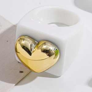 Detail of chunky white resin ring with large metallic gold heart charm in Y2K style