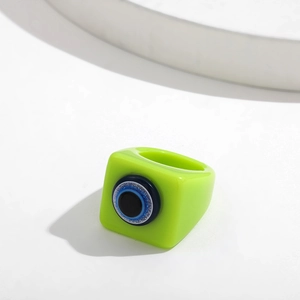 Macro detail of fluorescent green resin square ring featuring 3D blue evil eye element