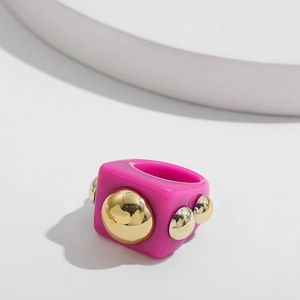 Detail of chunky magenta resin ring featuring golden hemisphere metal studs on white stand