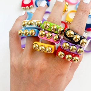 Close-up of vibrant resin rings featuring gold metallic sphere studs on model's fingers