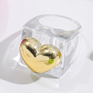 Macro detail of Y2K resin ring with shiny gold metal heart ornament on white background