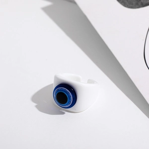 Macro detail of white resin evil eye open ring with blue glitter eye and flat band