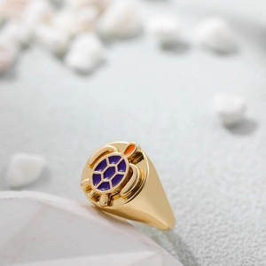 Makroaufnahme von 14K Gold Schildkrötenring mit lila Emaille auf einem weißen Stein Sockel