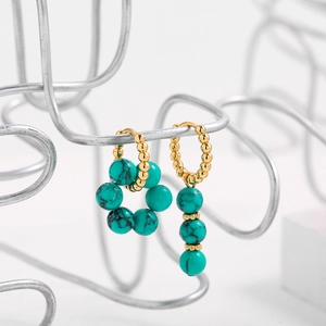Macro detail of asymmetric gold beaded earrings with blue turquoise flower and drop charms