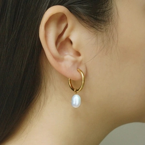 Gros plan d'une boucle d'oreille anneau doré avec perle ovale blanche sur un modèle