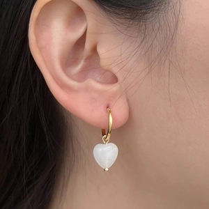 Détail d'une boucle d'oreille dorée avec pendentif coeur blanc porté sur un mannequin