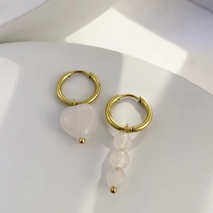 Détail de boucles d'oreilles cœur dorées asymétriques avec pierres et perles