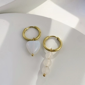 Détail de boucles d'oreilles dorées asymétriques avec cœur blanc et perles suspendues