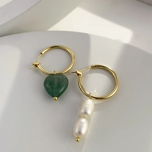 Détail de boucles d'oreilles dorées asymétriques avec cœur vert et perles blanches