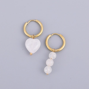 Détail de boucles d'oreilles dorées asymétriques avec pierre en cœur et perles rondes
