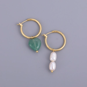 Détail de boucles d'oreilles dorées asymétriques avec pierre verte et perles