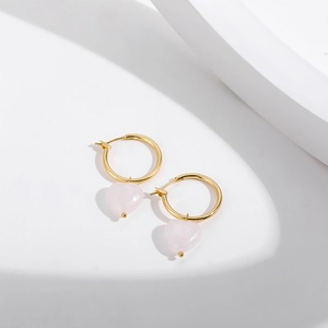Détail de boucles d'oreilles cœur rose avec créoles dorées sur fond blanc épuré