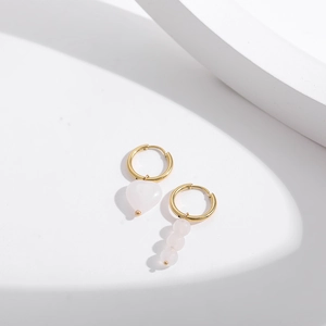 Détail de boucles d'oreilles asymétriques en pierre rose avec anneaux dorés et perles