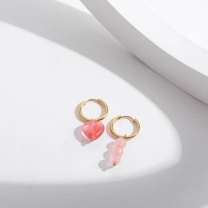 Détail de boucles d'oreilles pendantes asymétriques avec cœur et perles dorées