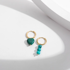 Détail de boucles d'oreilles dorées asymétriques avec cœur vert et pendentifs perlés