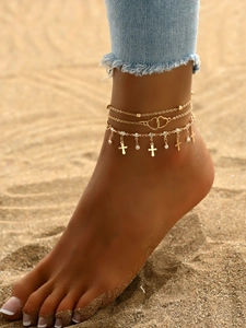 Nahaufnahme goldener Schicht-Fußkettchen mit Herz- und Kreuzanhängern auf dem Sand