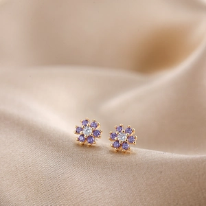 Detailed macro view of small flower stud earrings with purple crystals and gold base