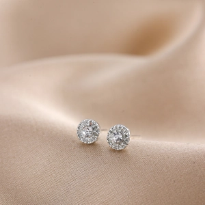 Macro detail of silver sunburst stud earrings with central cubic zirconia on silk