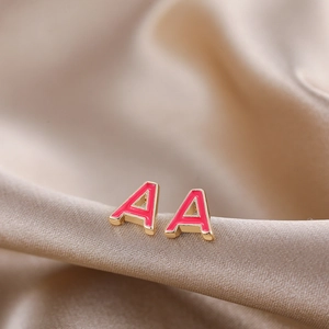 Macro shot of gold letter A stud earrings with pink enamel on champagne satin