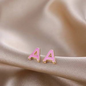 Macro shot of gold-plated letter A stud earrings with pink enamel on satin fabric