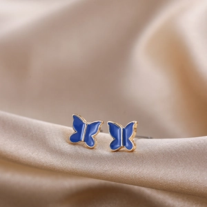 Macro shot of small blue enamel butterfly stud earrings with gold trim on silk