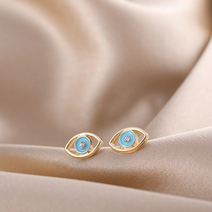 Detailed macro view of golden evil eye stud earrings with light blue enamel and small crystal