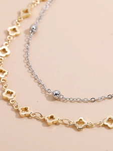 Detail einer mehrlagigen Goldkleeblatt-Kette und Silberperlen-Fußkettchen auf warmem Grund