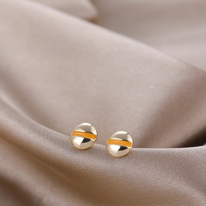 Detail view of gold screw head earrings with orange enamel on luxury champagne silk